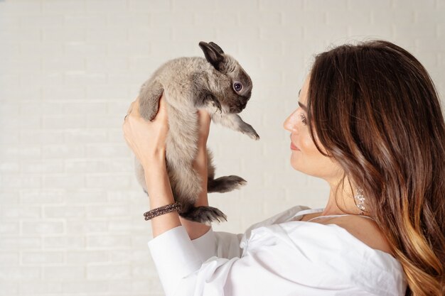 Hermosa joven sostiene un conejo gris lindo y esponjoso