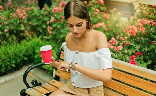 Hermosa joven sostiene una taza de café y mira el reloj de pulsera