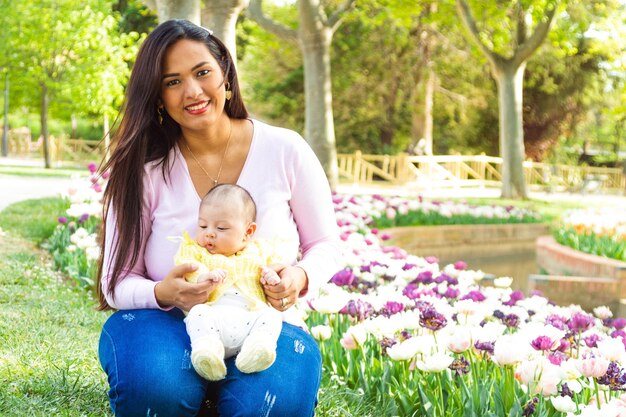 Foto hermosa joven con su bebé recién nacido en un parque lleno de tulipanes