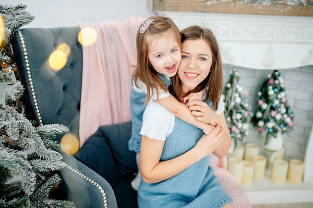 Hermosa joven y su encantadora hijita se abrazan en los mismos trajes sonriendo. Navidad