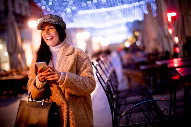 Hermosa joven con su teléfono móvil en la calle en Navidad