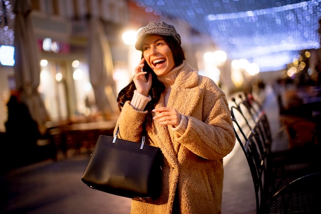 Hermosa joven con su teléfono móvil en la calle en Navidad