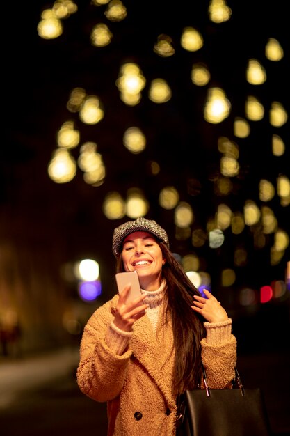 Foto hermosa joven con su teléfono móvil en la calle en navidad