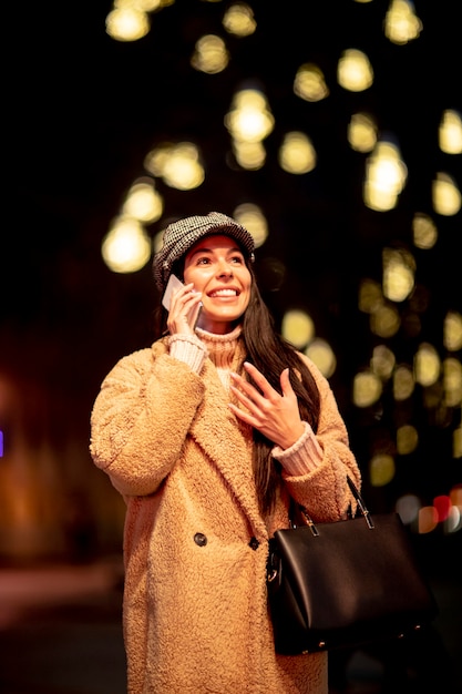 Hermosa joven con su teléfono móvil en la calle en Navidad