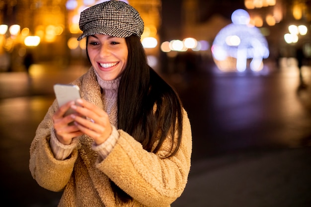 Hermosa joven con su teléfono móvil en la calle en Navidad