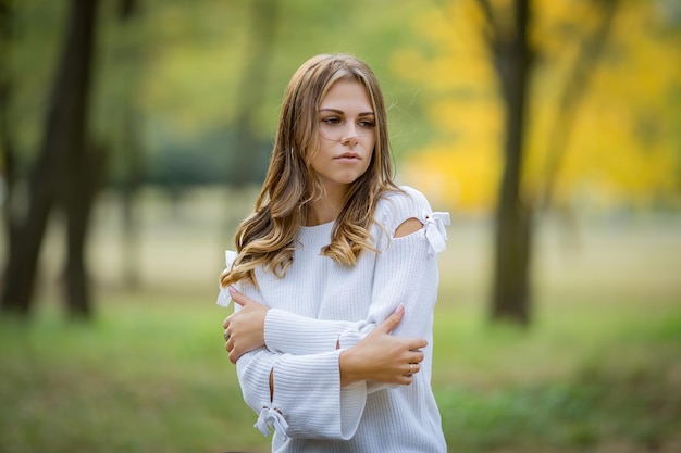 Hermosa joven con un suéter blanco en un parque de otoño Foto de alta calidad