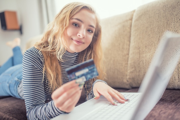 Hermosa joven con tarjeta de crédito comprando en línea en el sofá de la sala de estar.