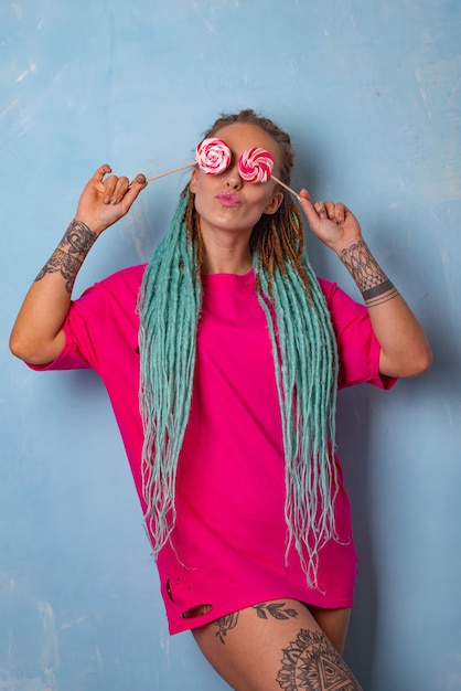 Hermosa joven con un tatuaje y rastas posando en una camiseta rosa con paletas de caramelo