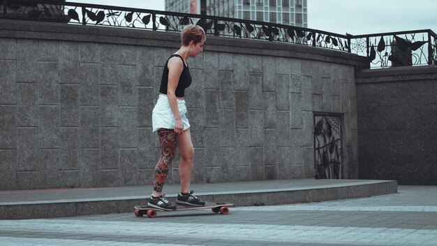 Hermosa joven con tatuajes con longboard en la ciudad. Ella tiene un tatuaje tradicional japonés.