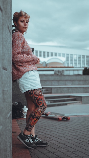 Hermosa joven con tatuajes con longboard en la ciudad. Ella tiene un tatuaje tradicional japonés.