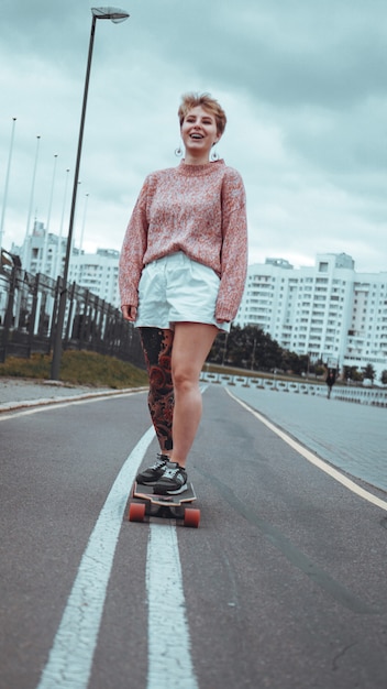 Hermosa joven con tatuajes con longboard en la ciudad. Ella tiene un tatuaje tradicional japonés.