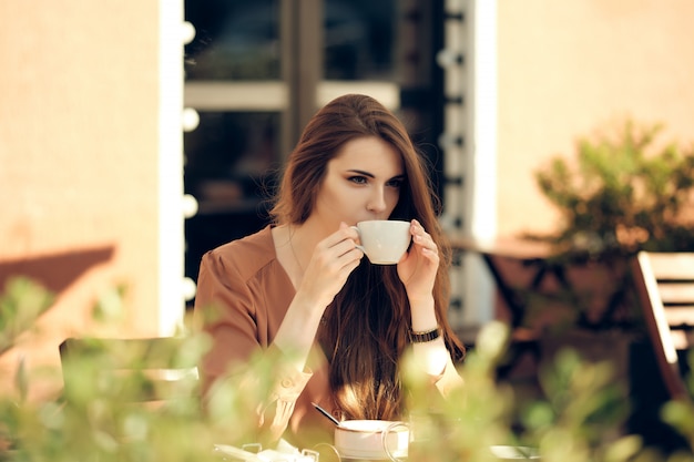 Hermosa joven tiene coffee break en medio del día soleado