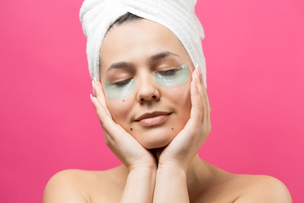 Hermosa joven en una toalla blanca en la cabeza usa parches de gel de colágeno debajo de los ojos