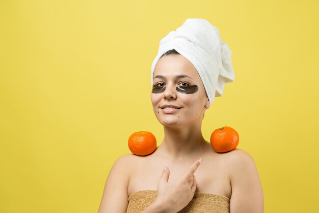 Hermosa joven en una toalla blanca en la cabeza usa parches de gel de colágeno debajo de los ojos