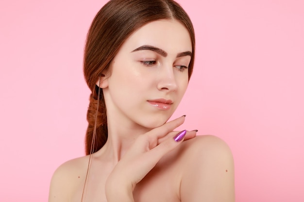 Hermosa joven tocando su piel perfecta sobre fondo rosa. Concepto de cuidado de la piel. Retrato de mujer de belleza con piel limpia. Modelo de moda linda belleza con maquillaje natural sobre fondo rosa