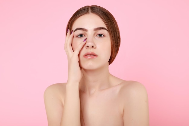 Hermosa joven tocando su piel perfecta sobre fondo rosa Concepto de cuidado de la piel Retrato de mujer de belleza con piel limpia Modelo de moda lindo de belleza con maquillaje natural sobre fondo rosa