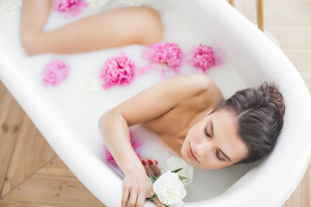 Hermosa joven tomando baño con flores y leche