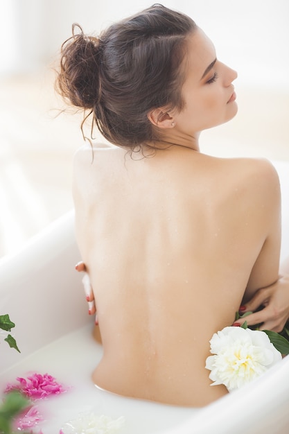 Hermosa joven tomando baño con flores y leche