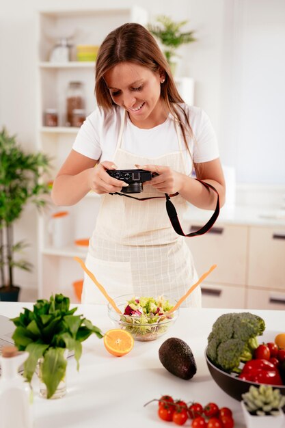 Hermosa joven tomando fotos de ensalada saludable con cámara fotográfica digital para su blog.