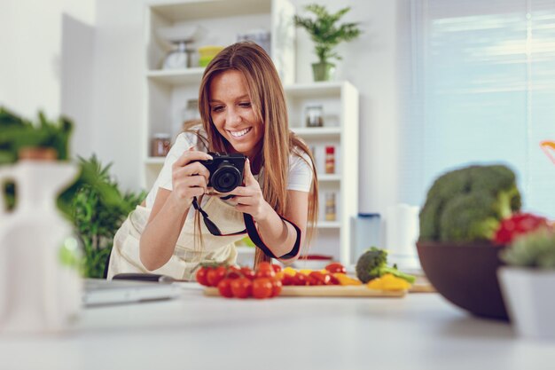 Hermosa joven tomando fotos de ensalada saludable con cámara fotográfica digital para su blog.