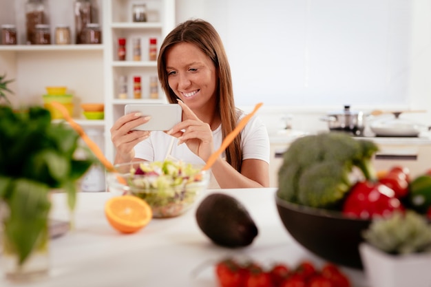 Hermosa joven tomando fotos de ensalada saludable con smartphone para su blog.