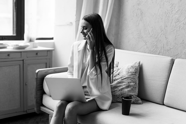 Hermosa joven trabajando en una computadora portátil mientras se sienta en la sala de estar, tomando café