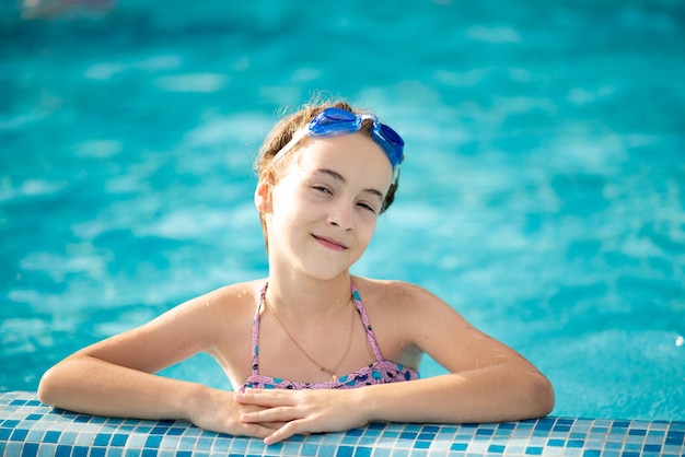 Una hermosa joven en traje de baño se baña en una piscina con agua azul clara en gafas de natación azules