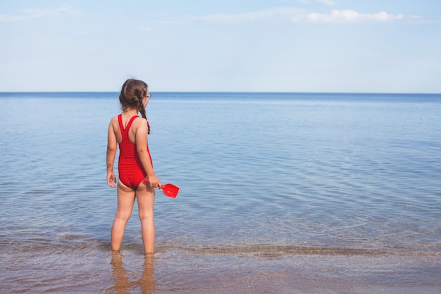 Hermosa joven en traje de baño rojo en la playa mirando las nubes