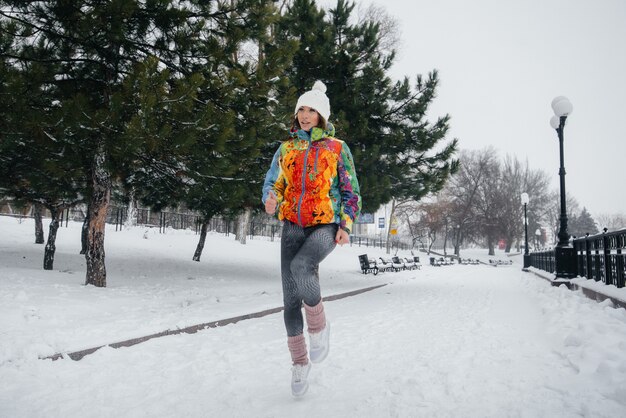 Una hermosa joven trota en un día helado y nevado. Deportes, estilo de vida saludable.