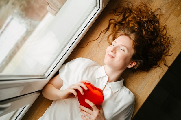 Hermosa joven tumbado junto a la ventana con un regalo para el día de San Valentín