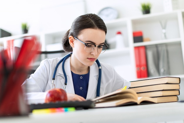 Una hermosa joven con una túnica blanca está sentada en el escritorio de la computadora con un marcador y un libro.