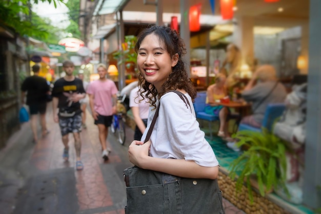 Hermosa joven turista asiática de vacaciones haciendo turismo y explorando en la calle Khao San por la noche