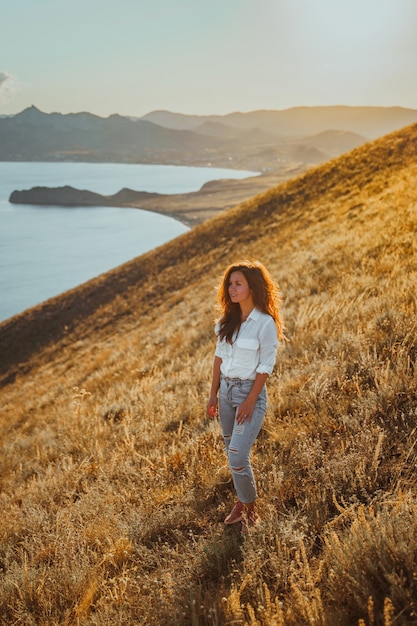 Una hermosa joven turista está sentada en la cima de una montaña y disfrutando de la vista de la puesta de sol