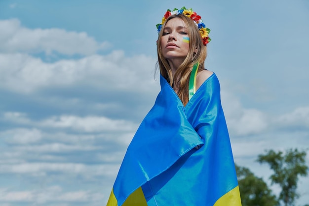 Hermosa joven ucraniana cubriendo con bandera nacional con cielo de fondo