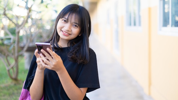 Hermosa joven usando un teléfono inteligente en la escuela, chica asiática, fondo naranja.