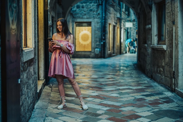 Hermosa joven usando un teléfono inteligente mientras camina por las calles de la ciudad en la costa durante la noche