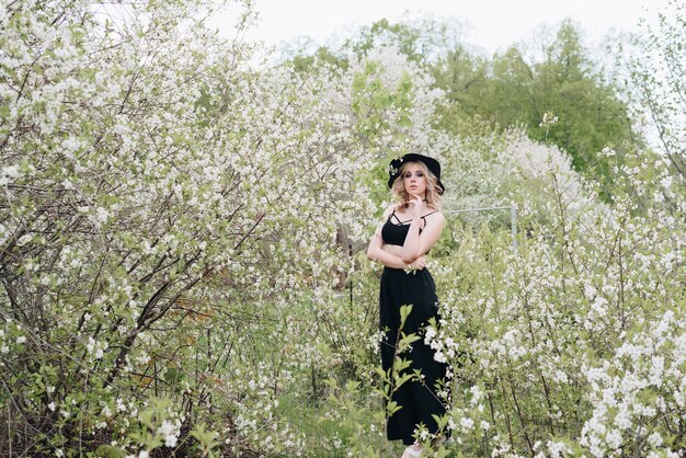 Una hermosa joven vestida de negro y un sombrero en un jardín floreciente en la primavera 1