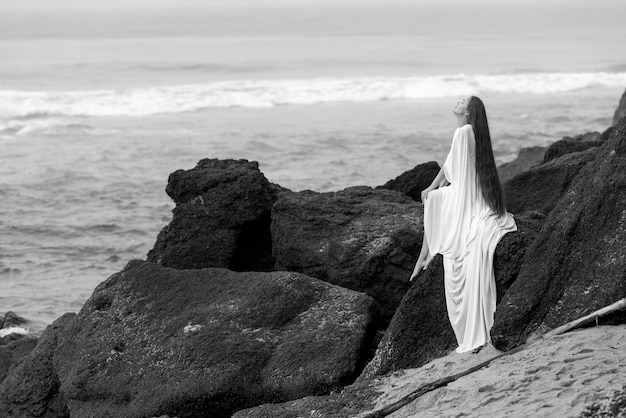 Hermosa joven vestida de novia y en la playa negra en Varkala, Kerala con roca alta