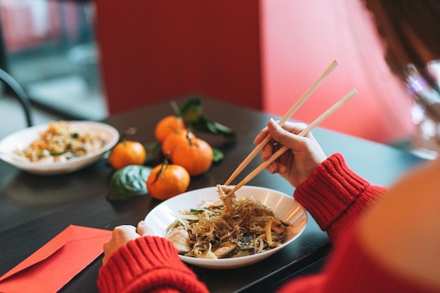 Hermosa joven vestida de rojo con un amigo comiendo fideos con palillos de bambú en el restaurante