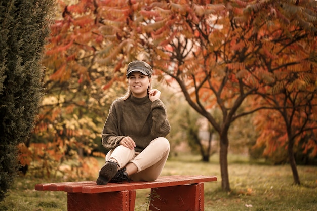 Hermosa joven vestida con ropa elegante, suéter verde y pantalón beige, en un parque de otoño con hermosos árboles