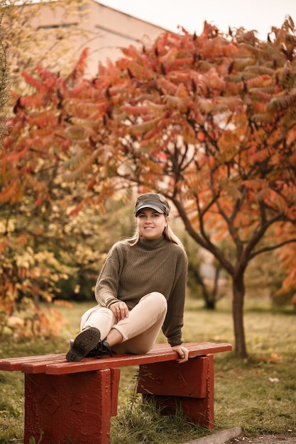 Hermosa joven vestida con ropa elegante, suéter verde y pantalón beige, en un parque de otoño con hermosos árboles