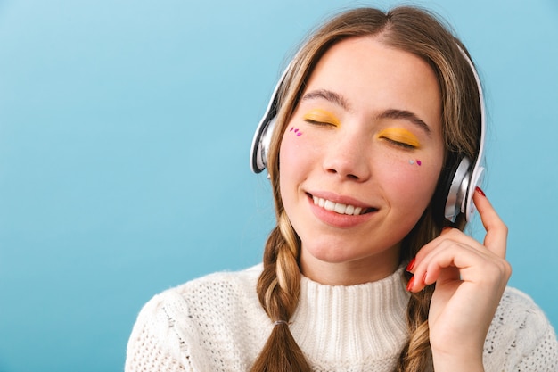 Hermosa joven vestida con ropa de invierno que se encuentran aisladas, escuchando música con auriculares