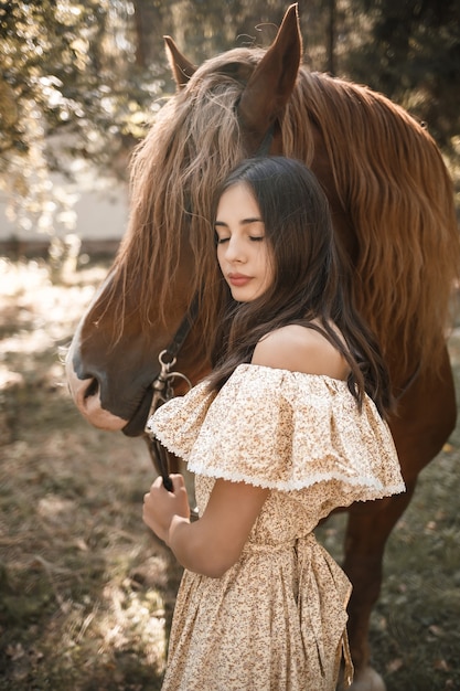 Una hermosa joven vestida con un vestido se encuentra cerca de un caballo en el bosque