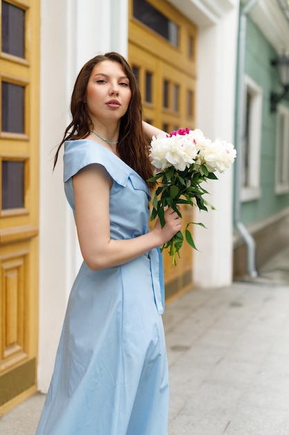 Una hermosa joven con un vestido azul con un ramo de peonías.