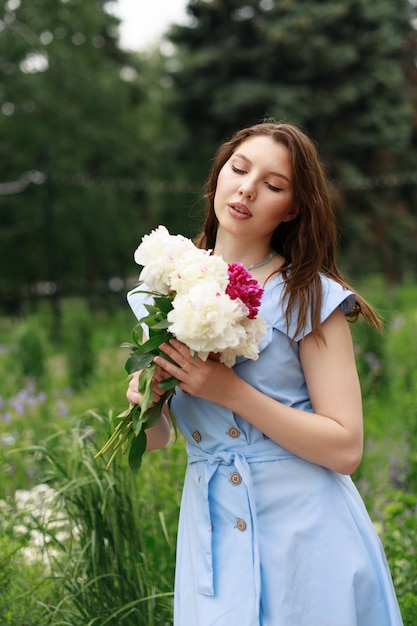 Una hermosa joven con un vestido azul con un ramo de peonías.