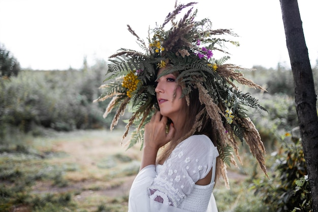 Una hermosa joven con un vestido blanco y una enorme corona de hierbas