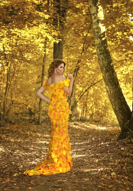 Hermosa joven con un vestido hecho de hojas de otoño en el parque en temporada de otoño. Foto de arte.