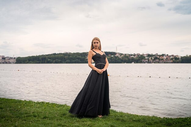 Hermosa joven con un vestido largo y oscuro en el fondo del cielo y el agua