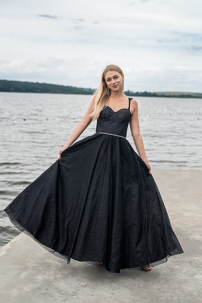 Hermosa joven con un vestido largo oscuro sobre fondo de cielo y agua, libertad