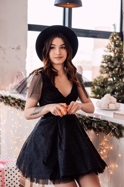 Hermosa joven con un vestido negro y un sombrero limpia una mandarina